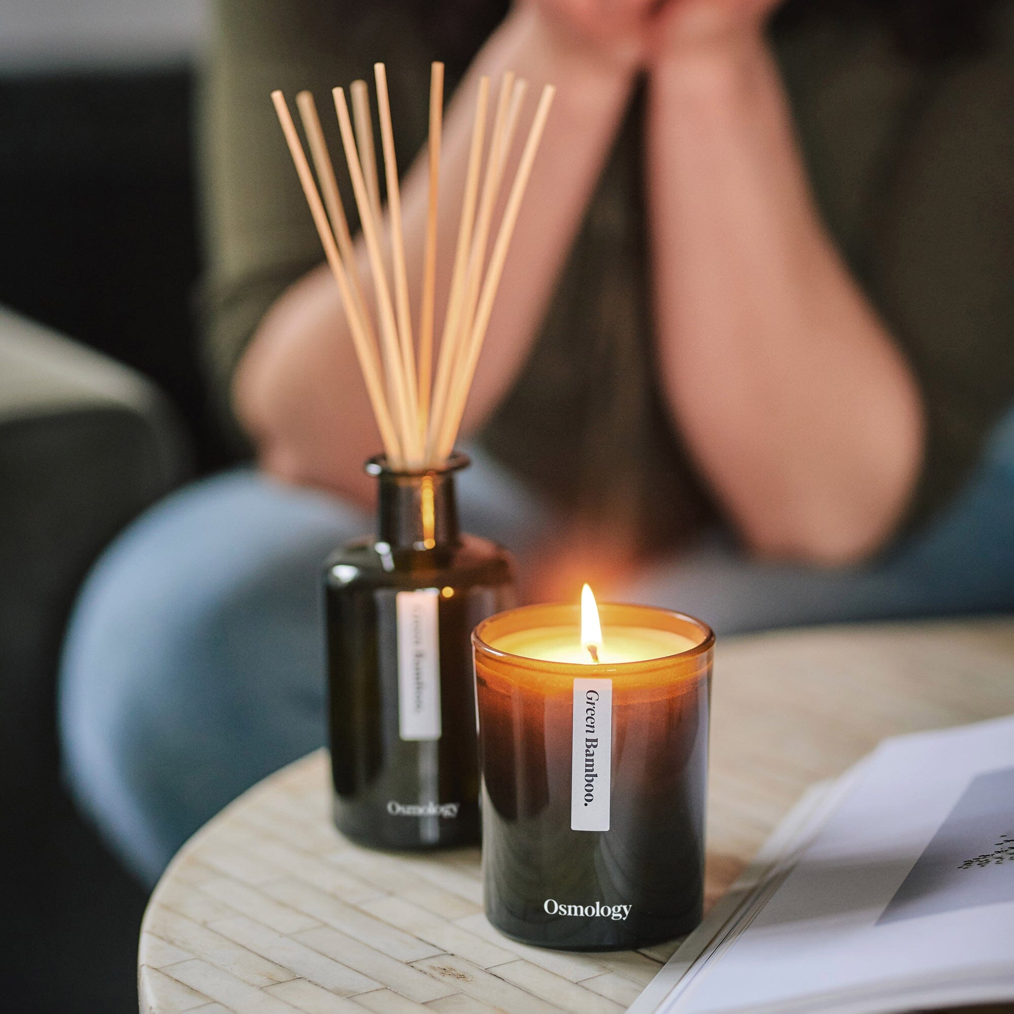 green bamboo candle and diffuser displayed on coffee table while person reads magazine