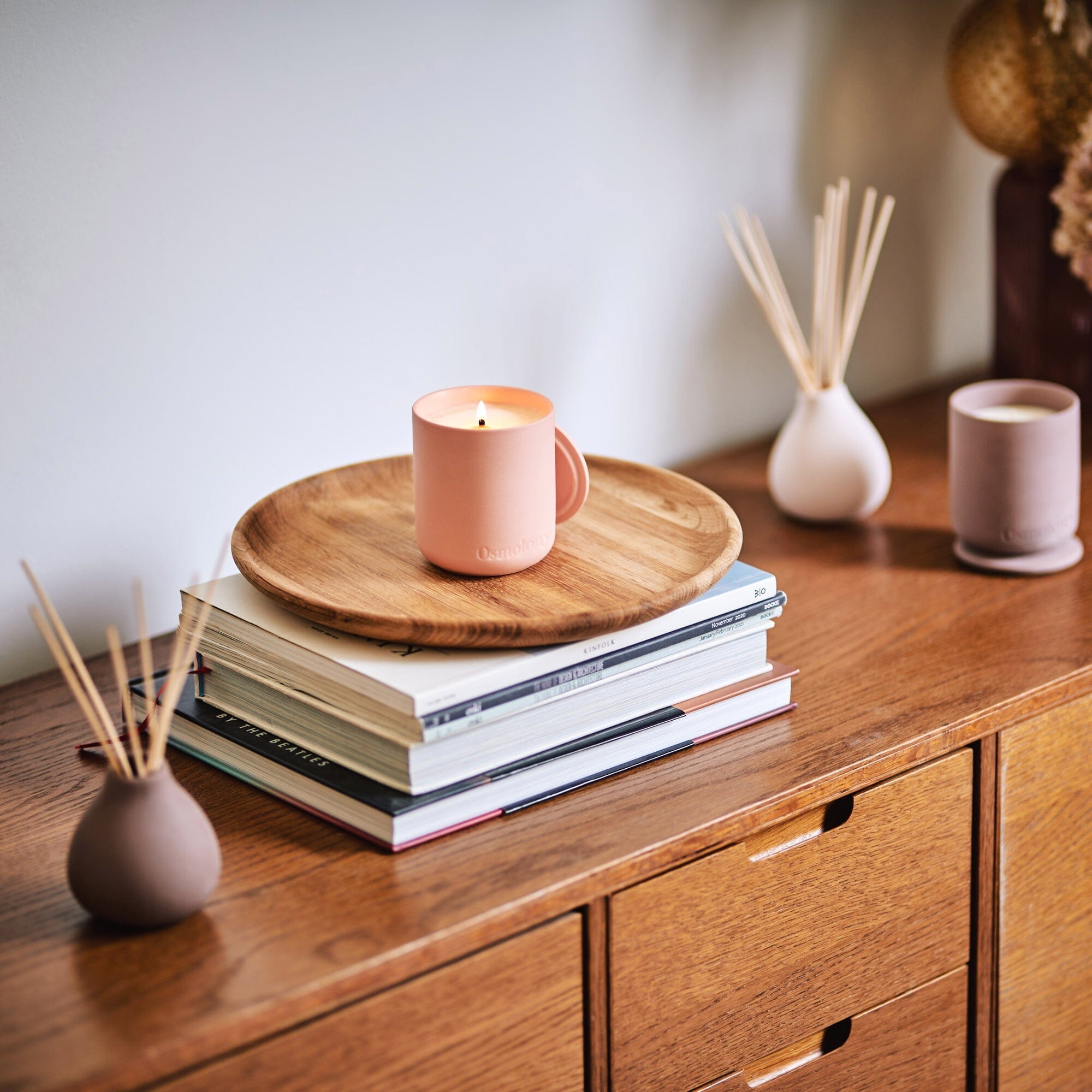 Ceramic peach candle by osmology lit and displayed decoratively on a sideboard with collection of ceramic candles and diffusers by osmology