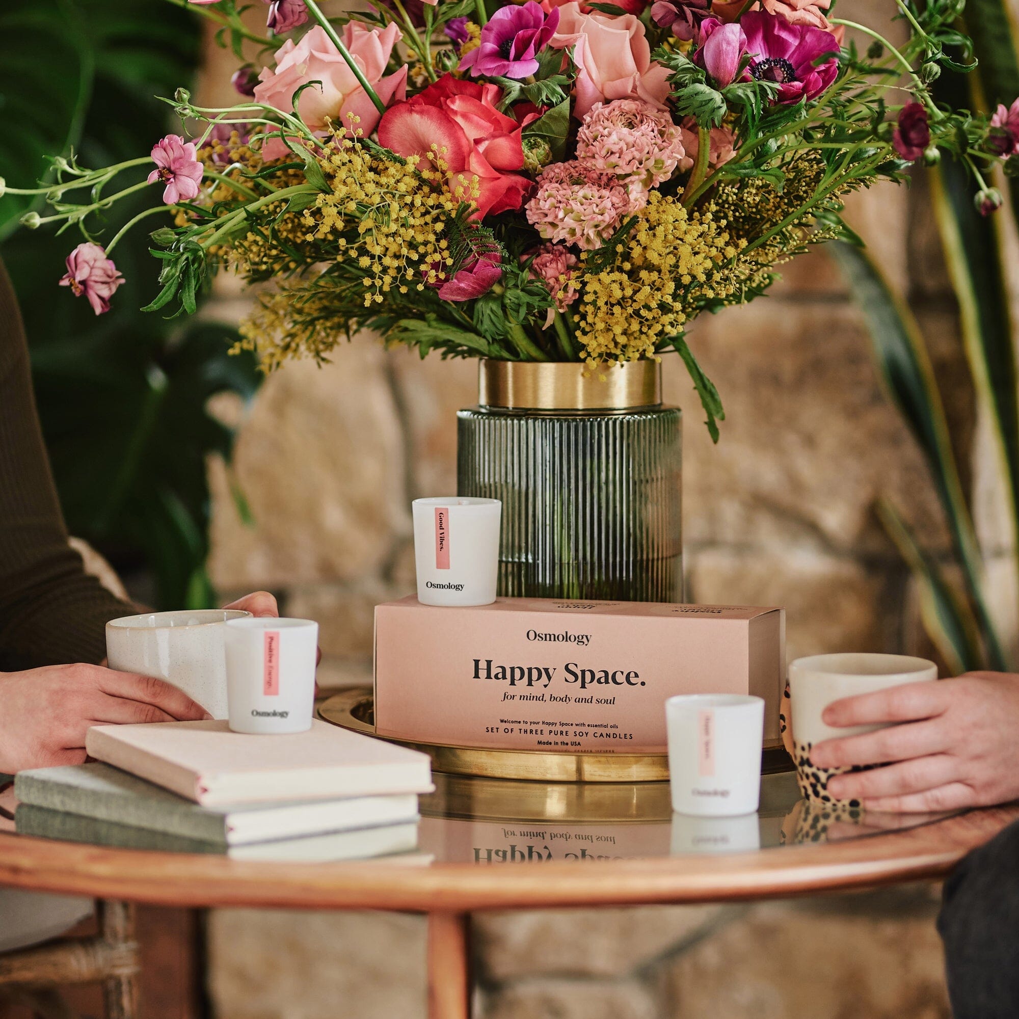 happy space candle gift set by osmology displayed on coffee table with two people having coffee next to a bunch of flowers