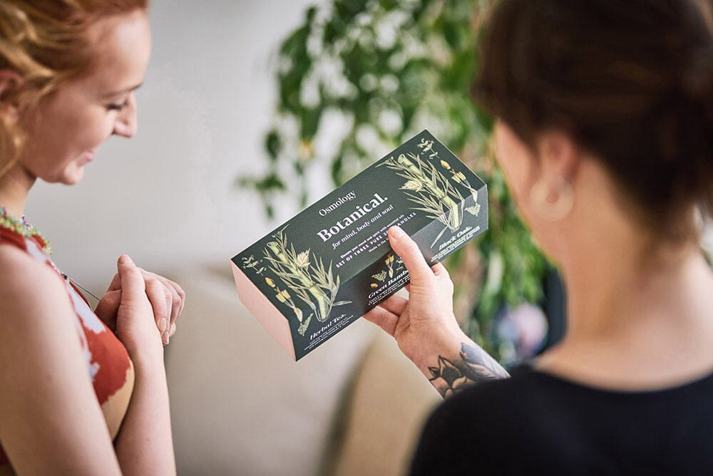 Osmology Botanical gift set held up by woman, another woman smiling receiving or giving gift