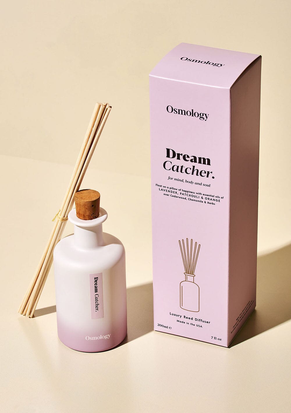 Osmology Dream Catcher reed diffuser with bunched reeds leaning against product packaging on cream background