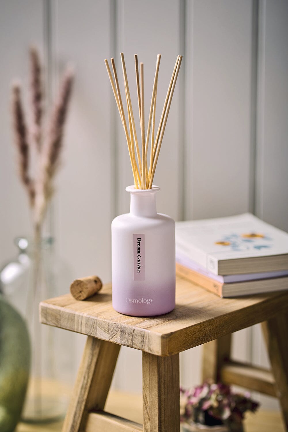 Osmology Dream Catcher reed diffuser placed on wooden stand with cork and books