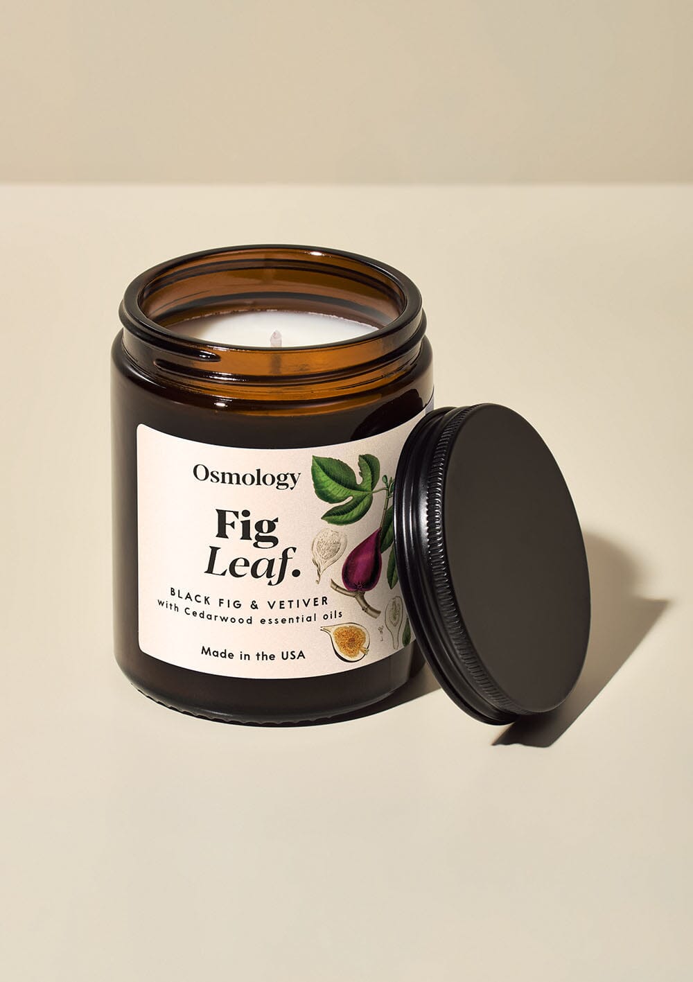 Osmology Fig Leaf jar candle, with lid open on a cream background