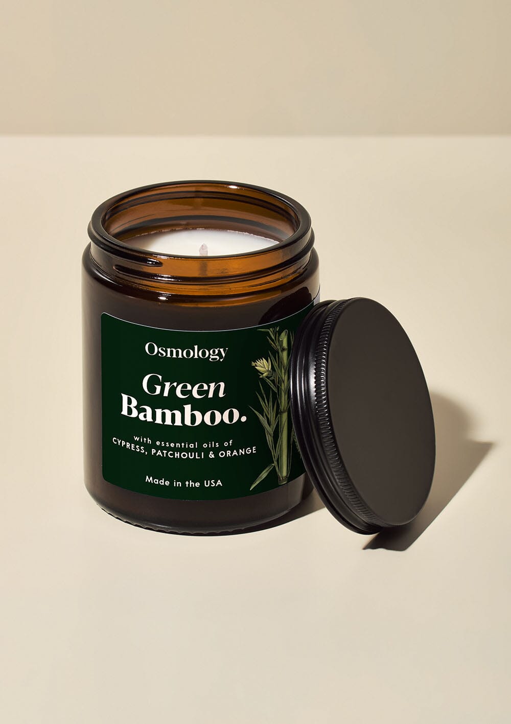 Osmology Green Bamboo jar candle with open lid on cream bcakground