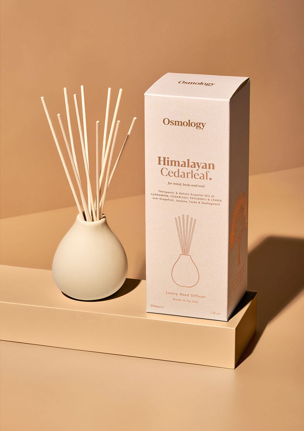 Osmology himalayan cedarleaf ceramic reed diffuser and product packaging on an orange background