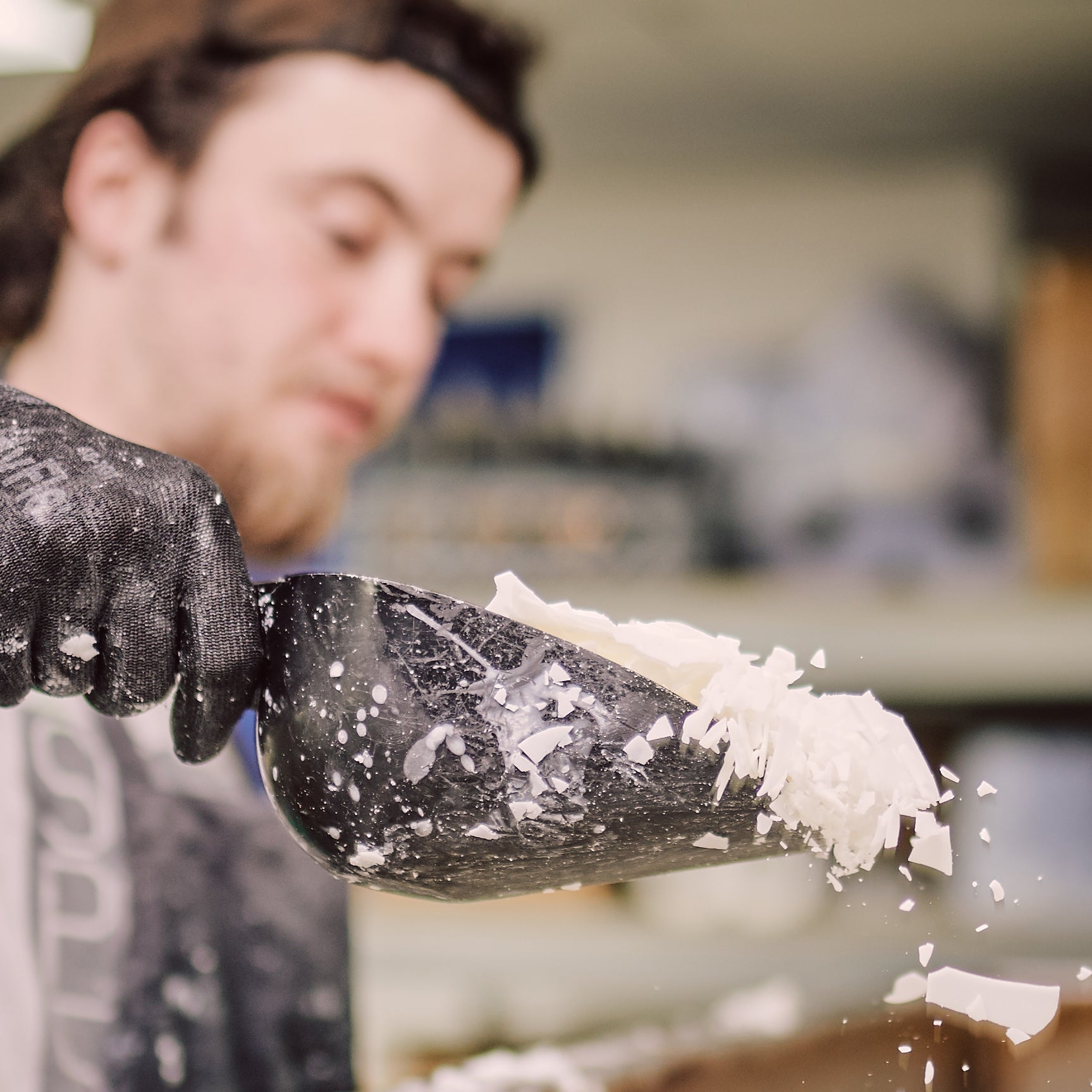 person pouring scoop fulls of candle wax flakes into a wax tank ready for melting